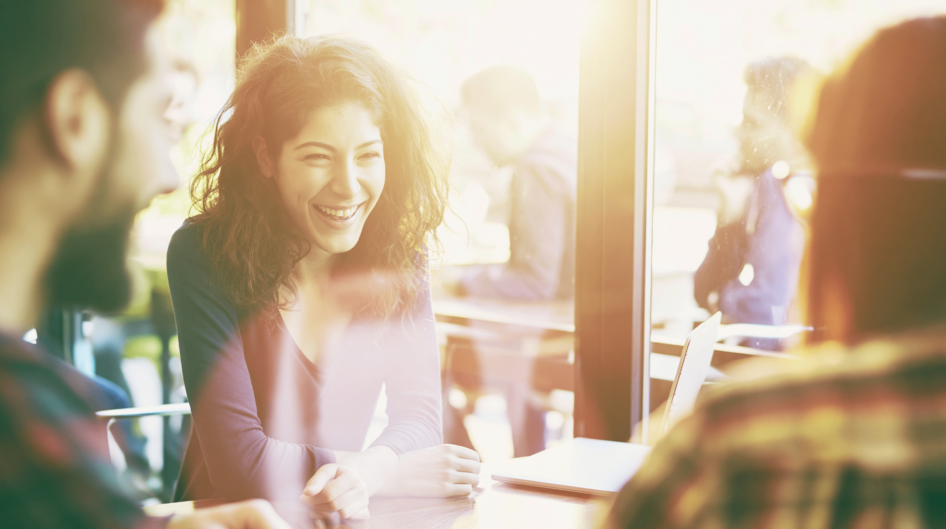 Woman laughing with friends in a sunlit cafe